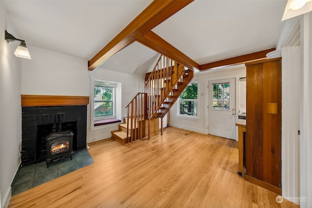 living room featuring a wood stove, light wood-type flooring, a wealth of natural light, and vaulted ceiling with beams