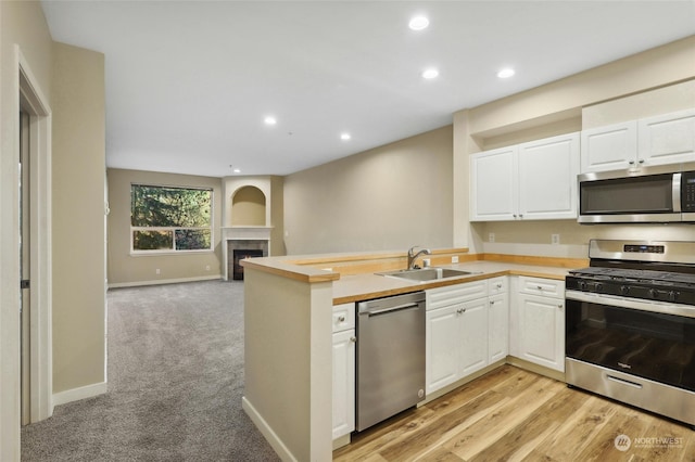 kitchen with kitchen peninsula, stainless steel appliances, sink, a tile fireplace, and white cabinetry