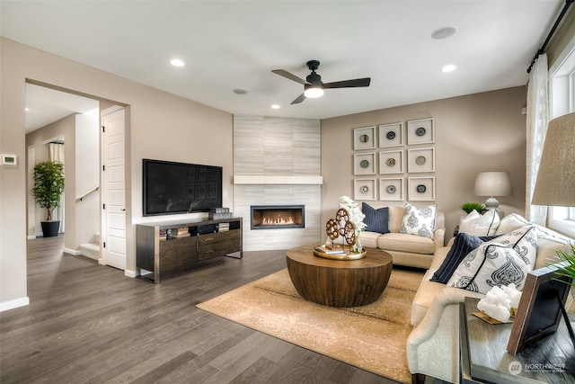 living room featuring a tile fireplace, ceiling fan, plenty of natural light, and dark wood-type flooring