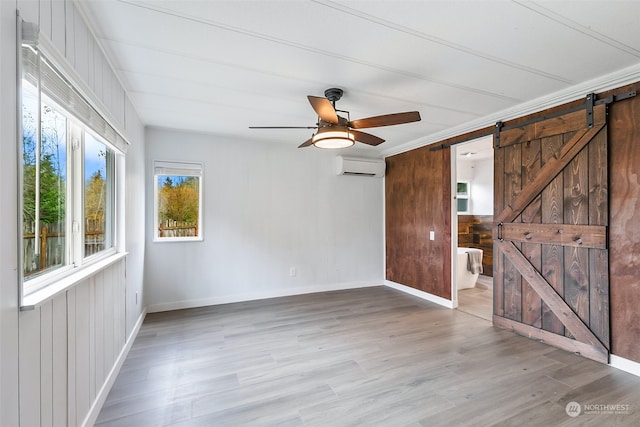 unfurnished room with ceiling fan, a barn door, a wall unit AC, and light wood-type flooring