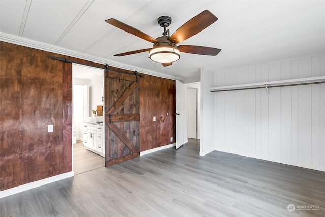 unfurnished bedroom featuring light hardwood / wood-style flooring, a barn door, ceiling fan, and ensuite bathroom