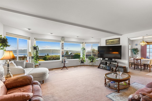 carpeted living room with plenty of natural light, beam ceiling, a water view, and an inviting chandelier