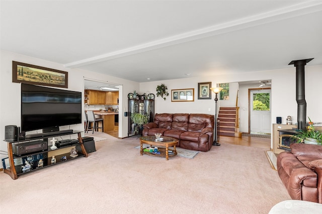 carpeted living room with beam ceiling and a wood stove