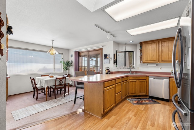 kitchen featuring kitchen peninsula, light wood-type flooring, stainless steel appliances, sink, and pendant lighting