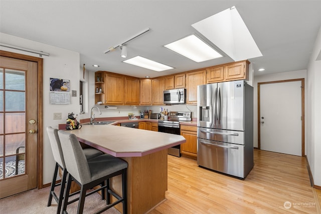 kitchen featuring kitchen peninsula, appliances with stainless steel finishes, a kitchen bar, track lighting, and sink