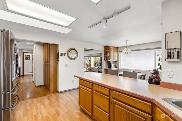 kitchen featuring a skylight, light hardwood / wood-style flooring, decorative light fixtures, stainless steel fridge with ice dispenser, and a chandelier