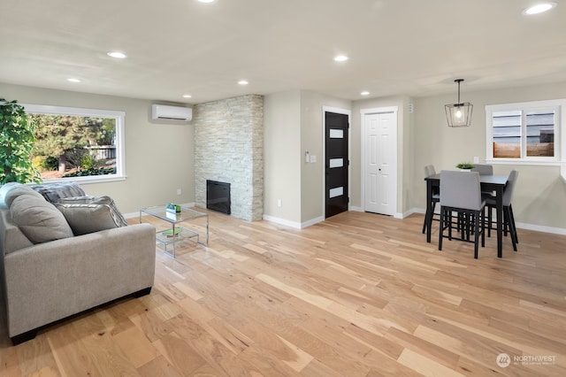 living room with light hardwood / wood-style floors, a stone fireplace, and a wall mounted air conditioner