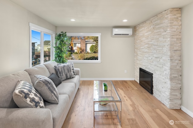 living room with a wall mounted AC, a fireplace, and light hardwood / wood-style flooring