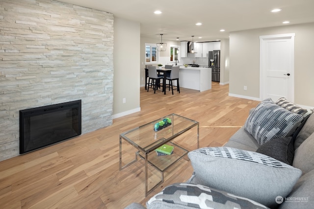 living room with a stone fireplace and light wood-type flooring