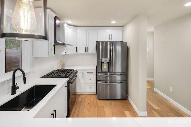 kitchen featuring stainless steel fridge, wall chimney range hood, sink, high end black range oven, and white cabinets