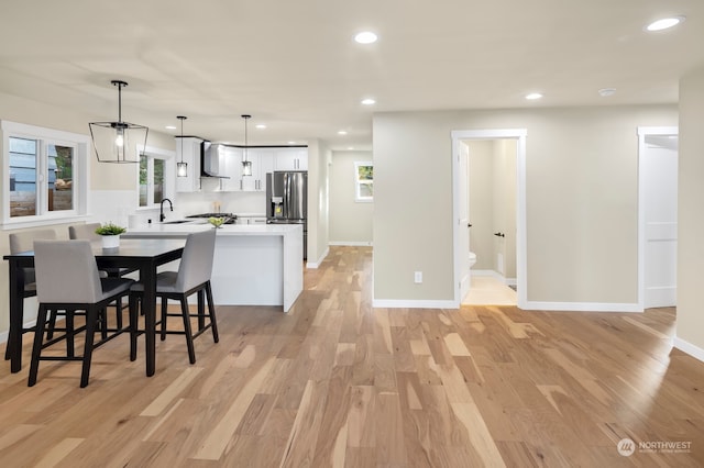 kitchen featuring pendant lighting, light wood-type flooring, wall chimney exhaust hood, and stainless steel fridge