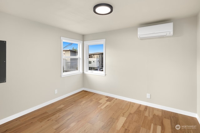 empty room with electric panel, light hardwood / wood-style floors, and a wall mounted AC