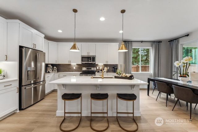 kitchen with a sink, a kitchen breakfast bar, backsplash, stainless steel appliances, and light countertops