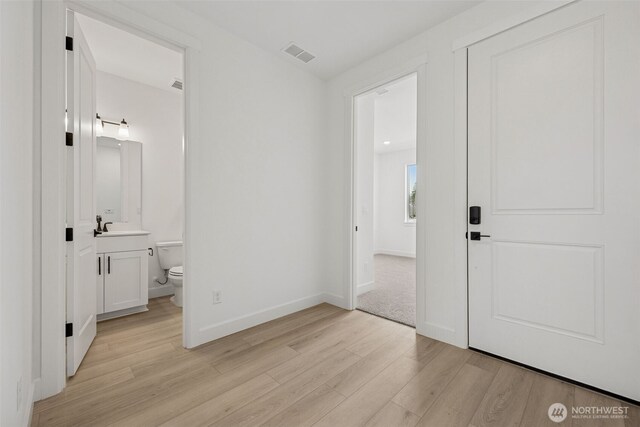 bedroom with baseboards, visible vents, a sink, light wood-type flooring, and connected bathroom