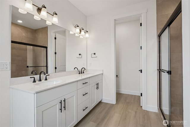 full bathroom with double vanity, a shower stall, wood finished floors, and a sink