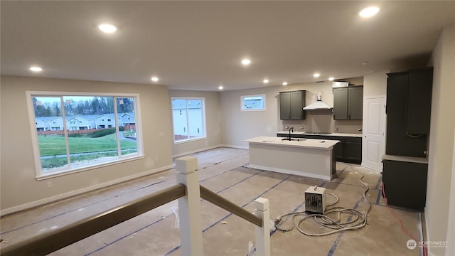 kitchen featuring an island with sink, sink, black electric stovetop, and wall chimney exhaust hood