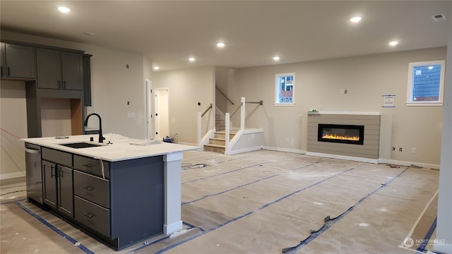 kitchen featuring sink, gray cabinets, dishwasher, light stone countertops, and an island with sink