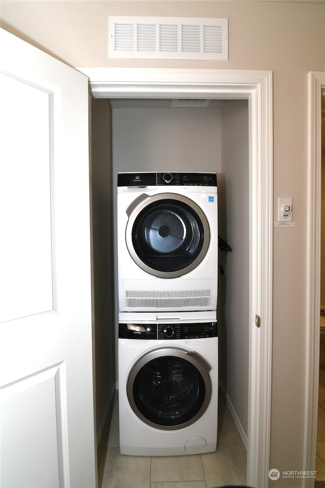 laundry area with light tile patterned floors and stacked washing maching and dryer