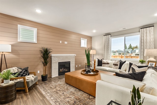 living room featuring a tiled fireplace, wood-type flooring, and wooden walls