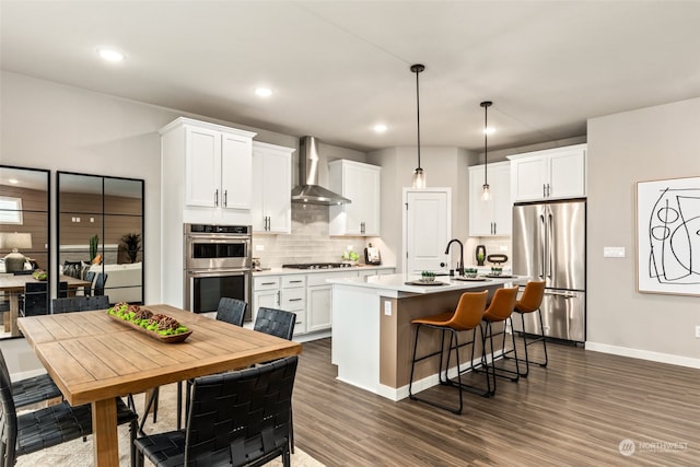 kitchen featuring stainless steel appliances, wall chimney range hood, a center island with sink, and white cabinetry