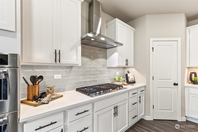 kitchen featuring tasteful backsplash, wall chimney range hood, appliances with stainless steel finishes, white cabinets, and dark wood-type flooring