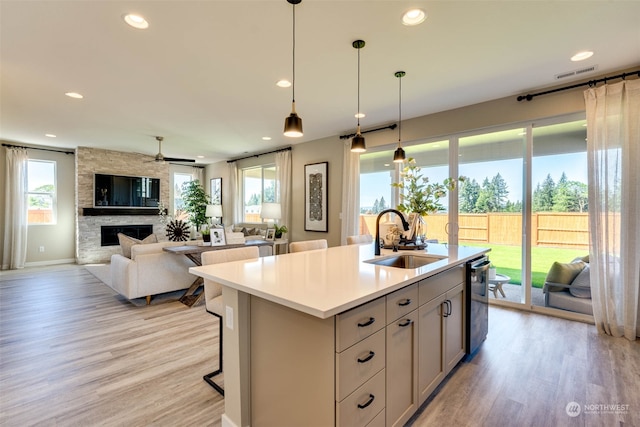 kitchen with sink, ceiling fan, a fireplace, an island with sink, and light hardwood / wood-style floors