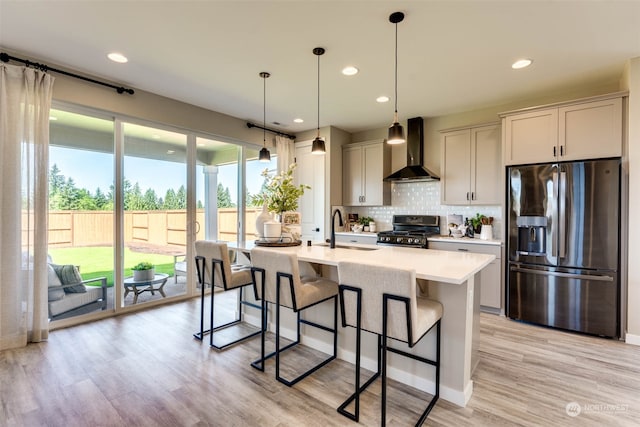 kitchen featuring sink, stainless steel refrigerator with ice dispenser, light hardwood / wood-style flooring, wall chimney exhaust hood, and range with gas stovetop