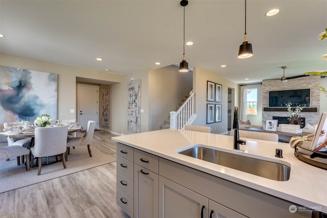 kitchen featuring pendant lighting, a stone fireplace, light wood-type flooring, and sink