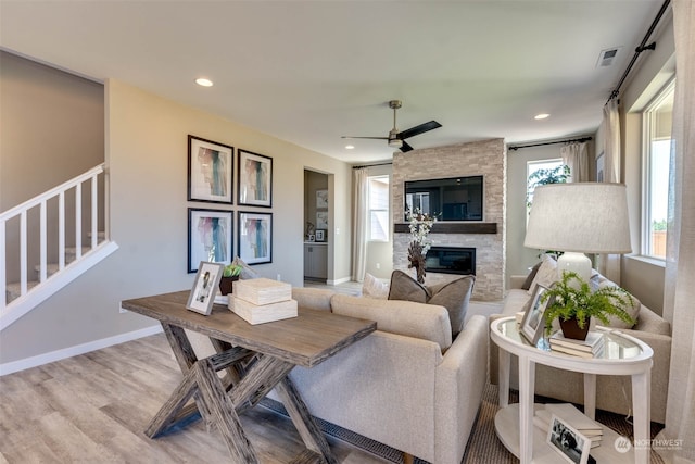 living room featuring ceiling fan, a stone fireplace, and light hardwood / wood-style flooring