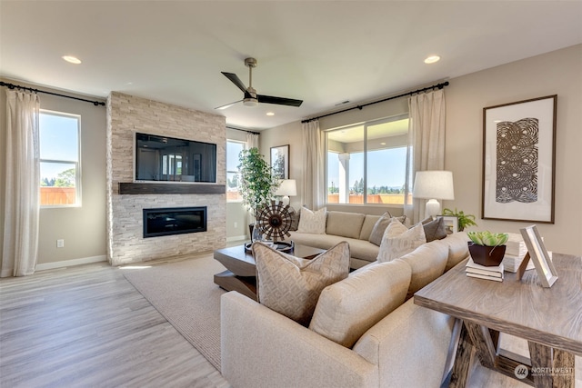 living room featuring light hardwood / wood-style flooring, a wealth of natural light, a stone fireplace, and ceiling fan