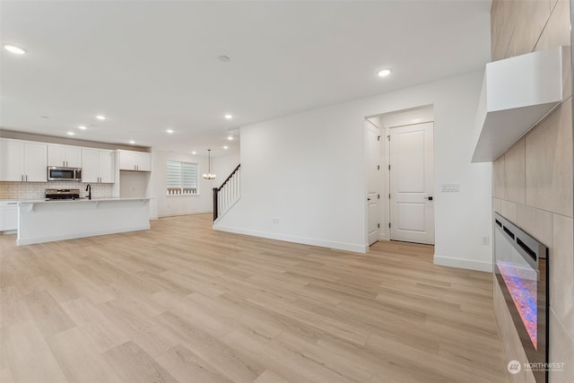 unfurnished living room with a large fireplace, light wood-type flooring, and a chandelier