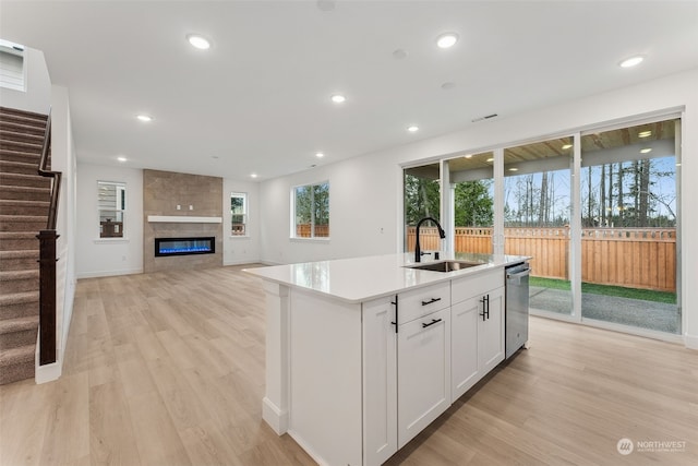 kitchen with a kitchen island with sink, a tile fireplace, sink, light hardwood / wood-style floors, and white cabinetry