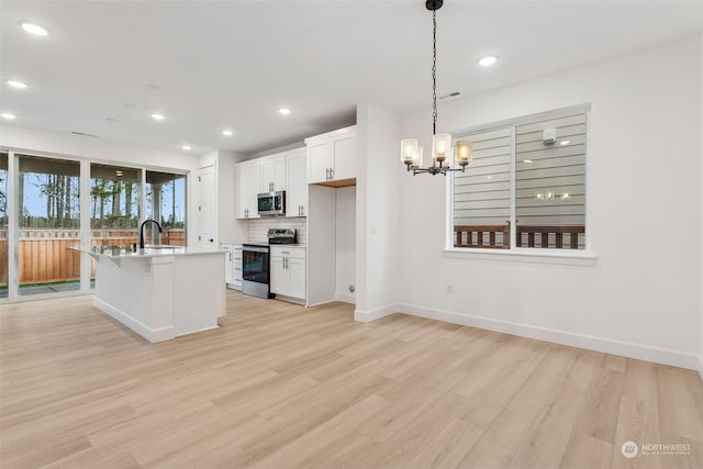 kitchen with white cabinets, pendant lighting, stainless steel appliances, and a kitchen island with sink