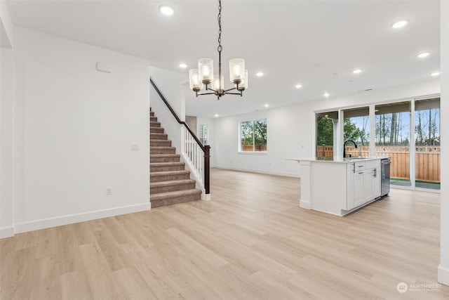 kitchen featuring pendant lighting, a kitchen island with sink, white cabinets, light hardwood / wood-style floors, and a chandelier