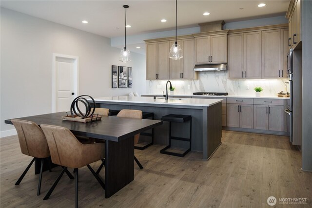 25708 64th Avenue Ct E Unit 4, Graham, WA 98338 - kitchen featuring under cabinet range hood, a sink, a kitchen island with sink, light wood-style flooring, and cooktop