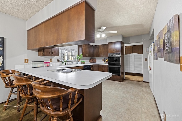 kitchen featuring kitchen peninsula, a kitchen bar, a textured ceiling, and ceiling fan