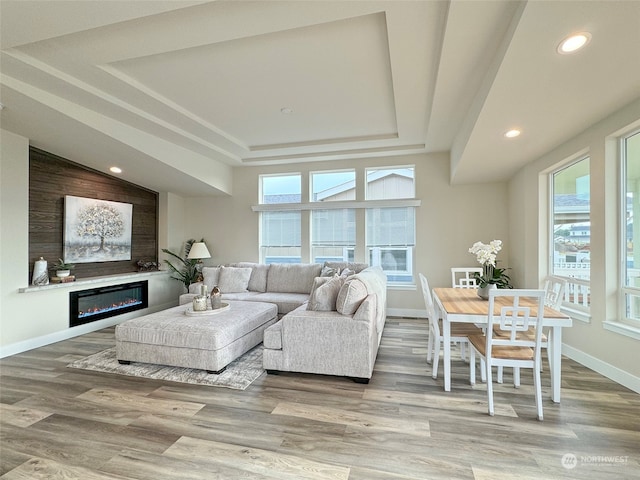 living room featuring wood-type flooring, a tray ceiling, and plenty of natural light