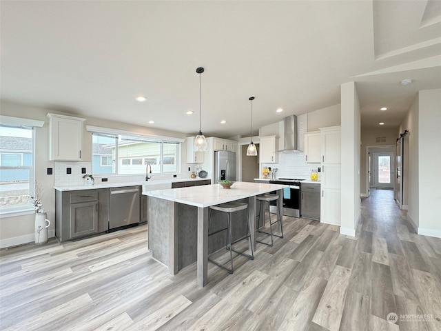 kitchen with a spacious island, light hardwood / wood-style flooring, wall chimney exhaust hood, a barn door, and stainless steel appliances