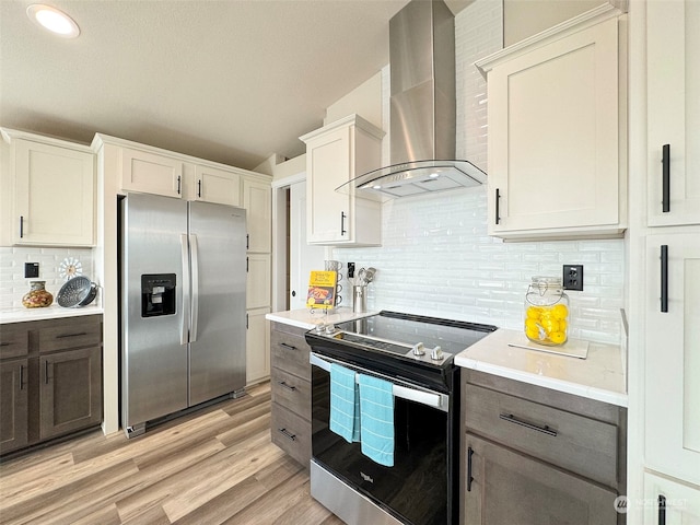 kitchen with decorative backsplash, appliances with stainless steel finishes, wall chimney exhaust hood, light hardwood / wood-style flooring, and white cabinetry