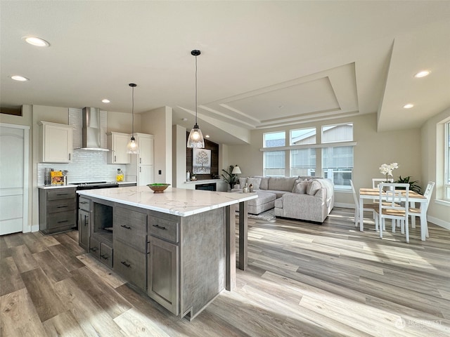 kitchen featuring white cabinetry, wall chimney exhaust hood, hanging light fixtures, wood-type flooring, and a kitchen island