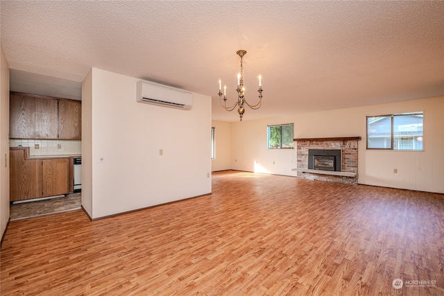 unfurnished living room featuring a chandelier, a textured ceiling, light hardwood / wood-style flooring, and a wall mounted air conditioner