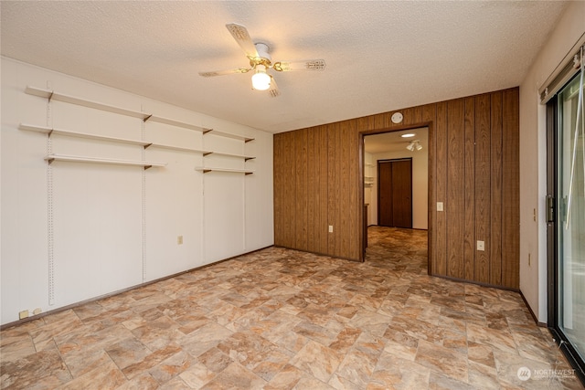 unfurnished bedroom featuring wood walls, a textured ceiling, and ceiling fan