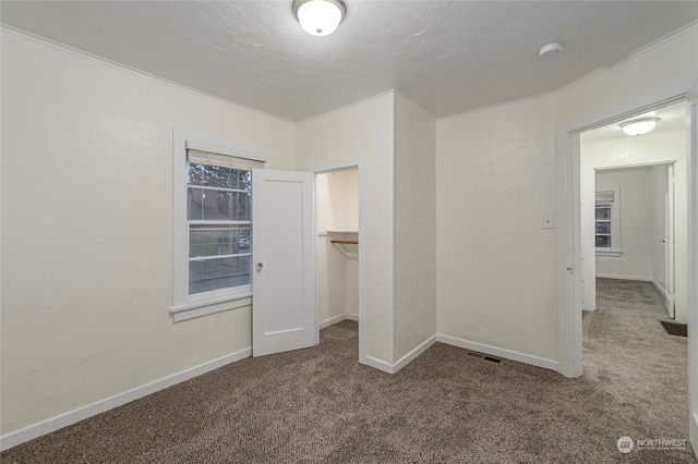 unfurnished bedroom with a textured ceiling, a walk in closet, carpet floors, and a closet