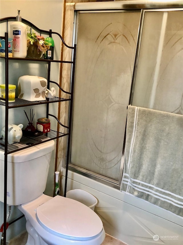 bathroom featuring toilet and shower / bath combination with glass door