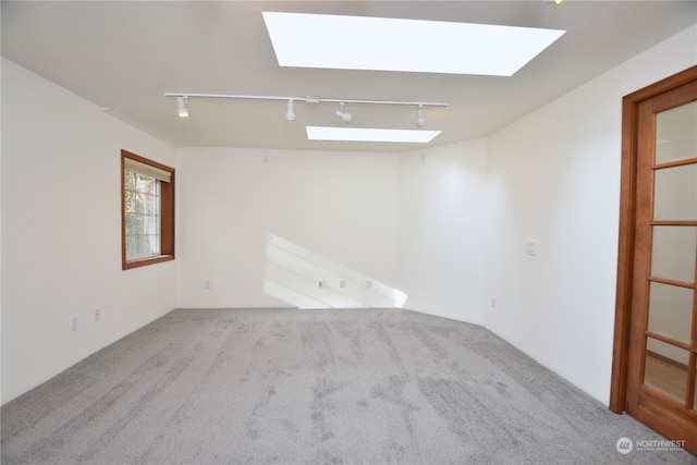 unfurnished room with track lighting, light colored carpet, and a skylight