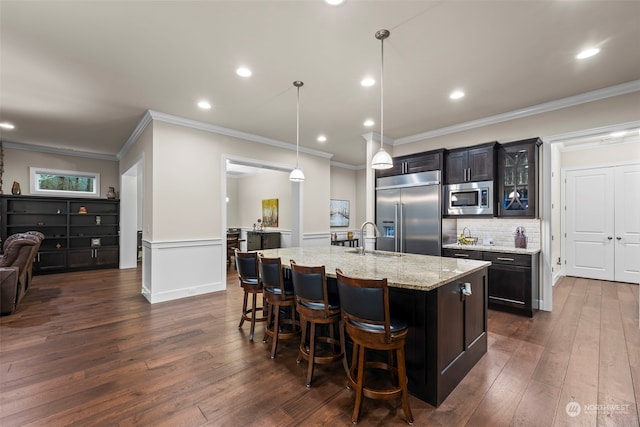 kitchen featuring sink, pendant lighting, built in appliances, a center island with sink, and dark hardwood / wood-style floors