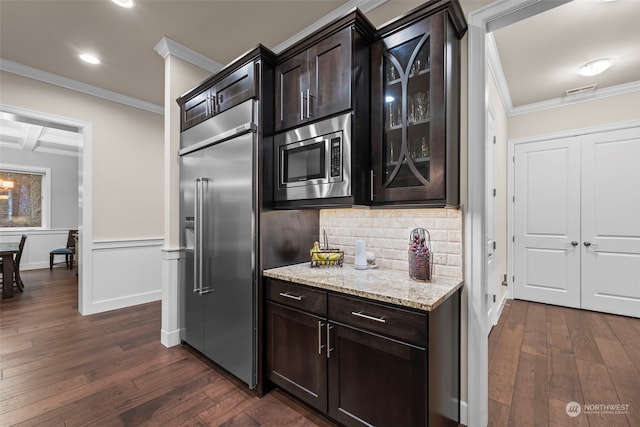 kitchen featuring ornamental molding, built in appliances, dark brown cabinetry, and dark wood-type flooring