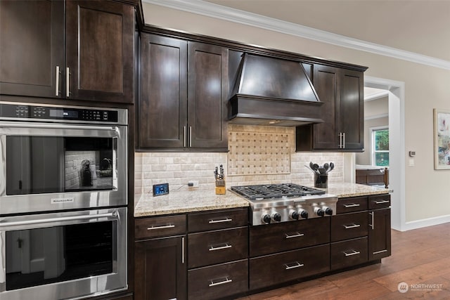 kitchen with appliances with stainless steel finishes, dark hardwood / wood-style flooring, custom range hood, dark brown cabinetry, and crown molding