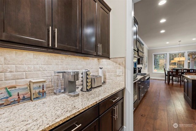 kitchen with light stone countertops, dark hardwood / wood-style flooring, dark brown cabinets, crown molding, and pendant lighting