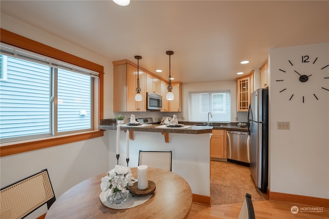 kitchen featuring kitchen peninsula, appliances with stainless steel finishes, decorative light fixtures, light hardwood / wood-style floors, and a breakfast bar area